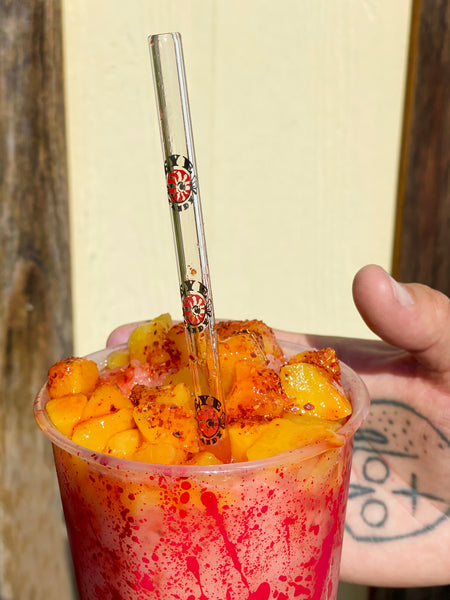 Cup of fruit juice with chili powder with glass straw inside. Straw features  Eyecandy company logo pattern with "EYECANDY" written in black