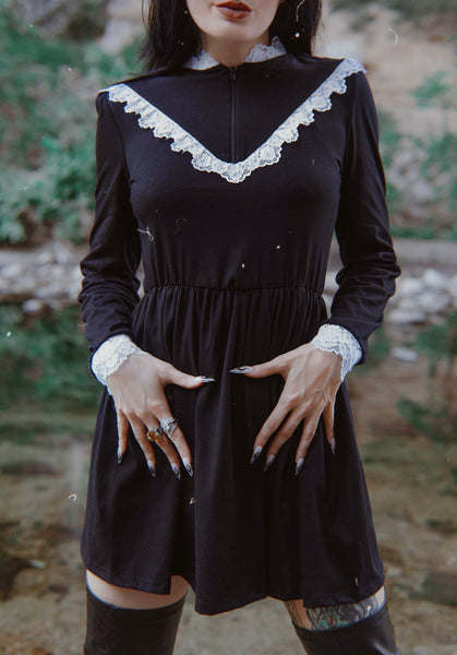 Black long sleeve, high neck, Victorian style dress with white lace trim neckline, cuffs and V shape trim from chest to shoulders. Black zipper down chest from neckline to V lace trim. Dress cinched at waist.