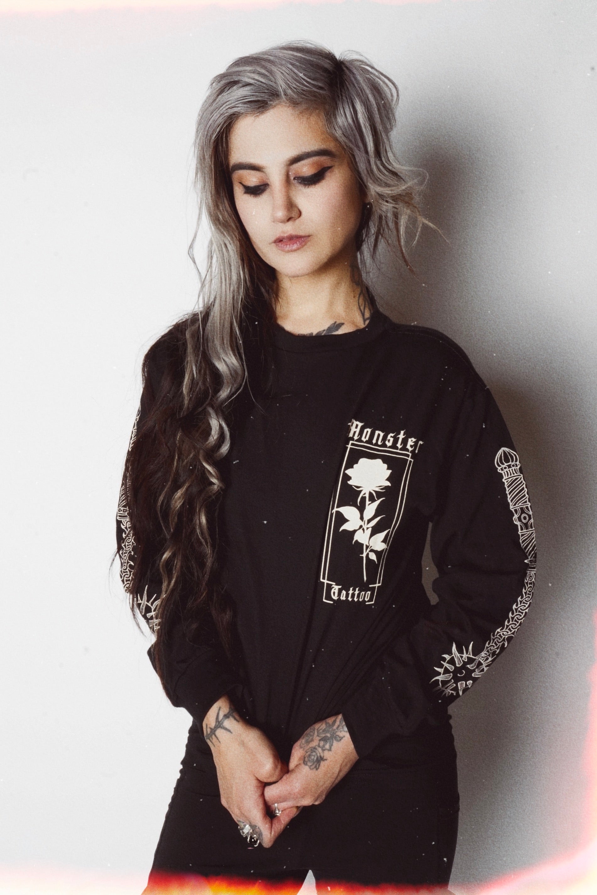 Black long sleeve white rose on left chest area with "Monster Tattoo" in white font. The sleeves have a print of ball and chain