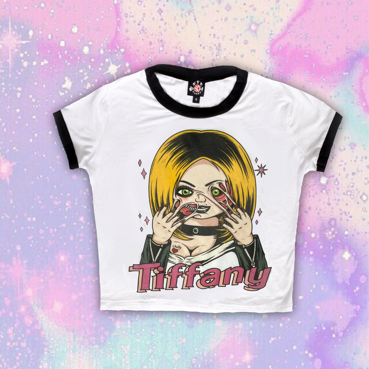White ringer tee with black trim. Features Tiffany from the movie Bride of Chucky wearing black jacket and choker with her face melting. Black "Chucky" and red heart tattoo on her breast and pink sparkles in background of image. Inscription reads "Tiffany" in pink.