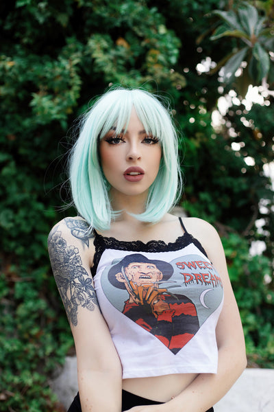 White tank top with thin black straps and black lace trim neckline. Features Freddy Krueger with one hand on face inside heart shape. Also features white crescent moon in heart shape. Inscription reads "SWEET DREAMS" in red. 