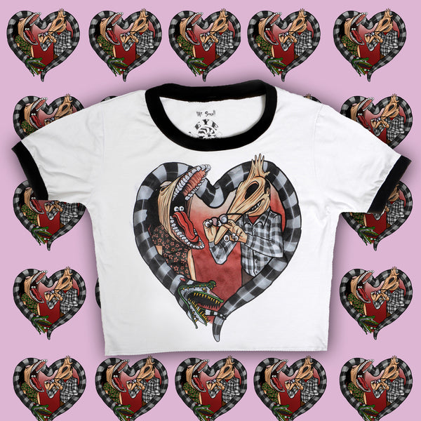 White ringer tee with black trim. Features image of Barbara and Adam from the movie Beetlejuice. Barbara has face stretched with mouth open, tongue sticking out and eyes in mouth. Adam has his face stretched out with eyeballs on his fingers and glasses in hand. Black and white Beetlejuice snake around Adam and Barbara in the shape of a heart.