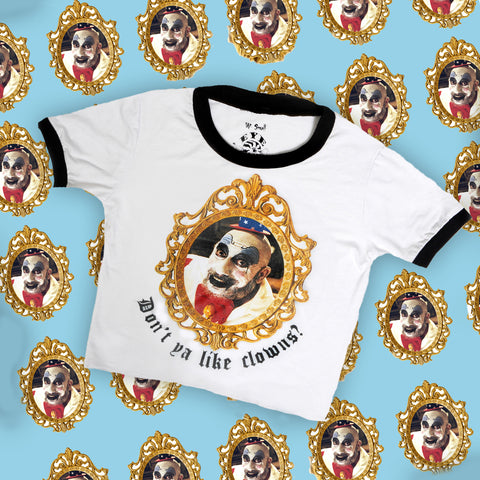 White ringer tee with black trim. Print features clown picture inside gold frame. Inscription reads "Don't ya like clowns?" in black.