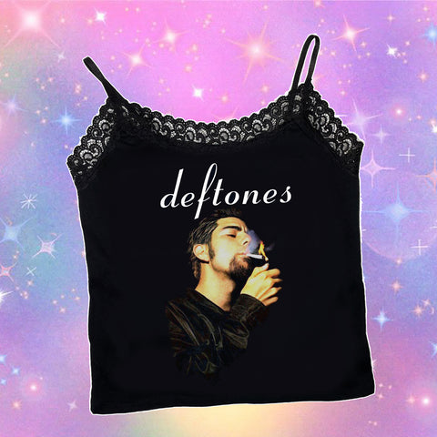 Black thin strap slightly cropped tank top with black lace trim neckline. Print features musician, Chino Moreno, lighting up cigarette. Inscription reads "Deftones" written in white font.