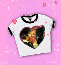 white ringer tee with black trim. Features Nancy from the movie "The Craft" and Lydia from "Beetlejuice" kissing inside a heart shape.