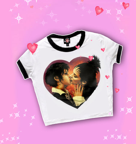 white ringer tee with black trim. Features Nancy from the movie "The Craft" and Lydia from "Beetlejuice" kissing inside a heart shape.
