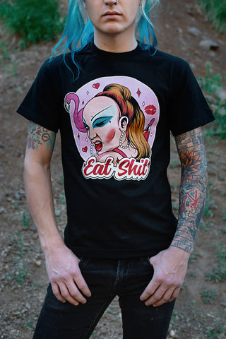 Black short sleeve t-shirt. Features woman with makeup winking her eye. Lipstick, hearts, and flamingo behind her with a pink background. Inscription reads "Eat Shit" written in pink font.