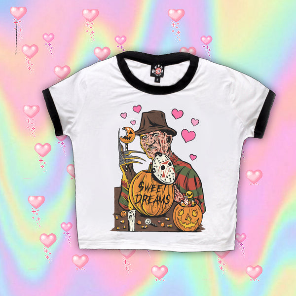 White ringer tee with black trim. Print is Freddy Krueger eating lollipop and has pumpkins and candy in front of him. On the pumpkins is a Jason hockey mask and pink hearts are behind Freddy. Center pumpkin says "Sweet Dreams" in black font