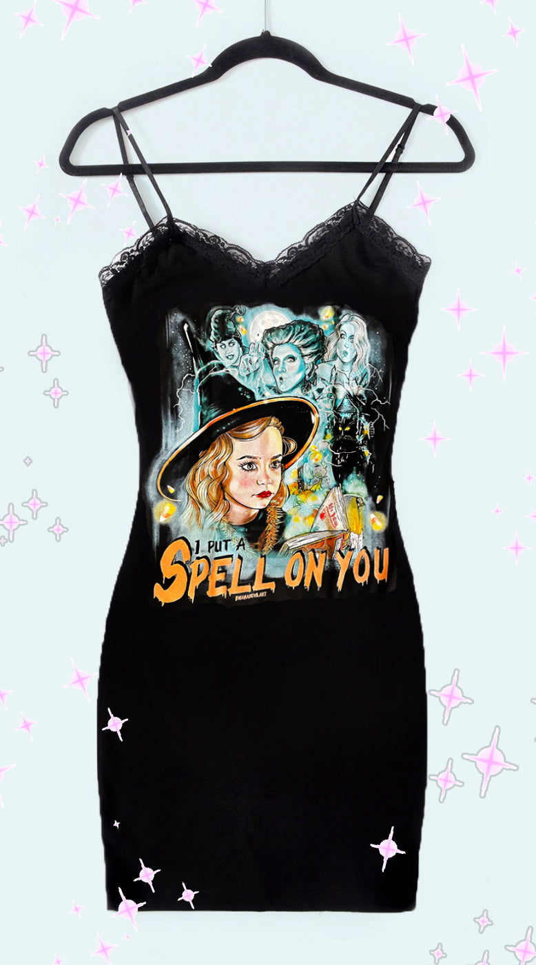 Black thin strap mini dress with black lace trim neckline. Features image of the Sanderson sisters and black cat with Dani Dennison wearing a witch hat. Inscription reads "I PUT A SPELL ON YOU" in black and orange.
