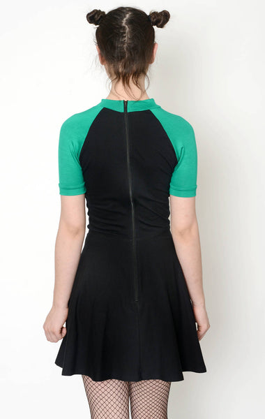 Back view of black baby doll style dress with green short sleeves and green trim neckline. Back of dress has black zipper along back. 