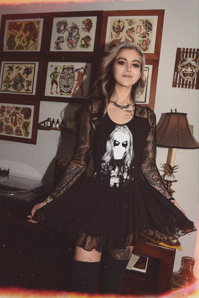 Black ballerina style dress with long sheer sleeves and sheer trim on bottom of skirt. Black and white print shows man with corpse paint.