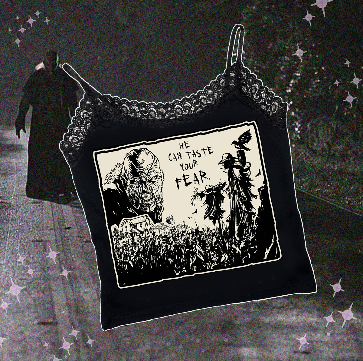 Black thin strap tank top with black lace trim neckline. Features black and white image of creeper from movie Jeepers Creepers face over house and cornfield with scarecrows and crows. Inscription reads "HE CAN TASTE YOUR FEAR" in black.