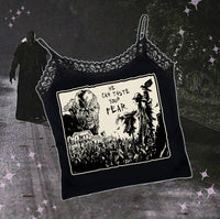 Black thin strap tank top with black lace trim neckline. Features black and white image of creeper from movie Jeepers Creepers face over house and cornfield with scarecrows and crows. Inscription reads "HE CAN TASTE YOUR FEAR" in black.