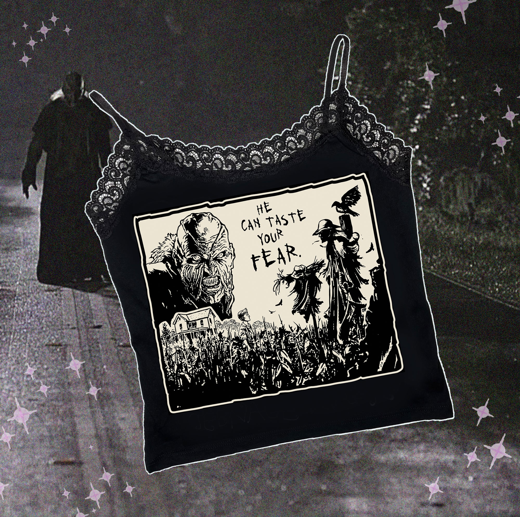 Black thin strap tank top with black lace trim neckline. Features black and white image of creeper from movie Jeepers Creepers face over house and cornfield with scarecrows and crows. Inscription reads "HE CAN TASTE YOUR FEAR" in black.