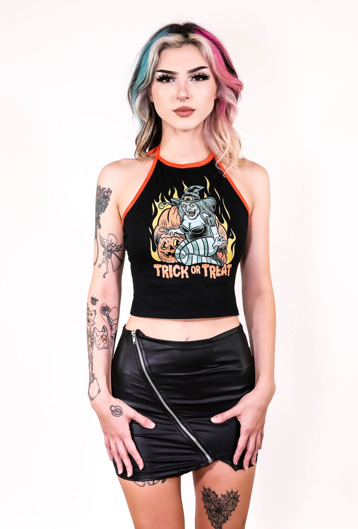 Black halter top with thin orange tie around neck straps and orange trim. Features green witch with an evil smile kneeling by orange pumpkins with yellow flames in background. Inscription reads "Trick or Treat" in orange.