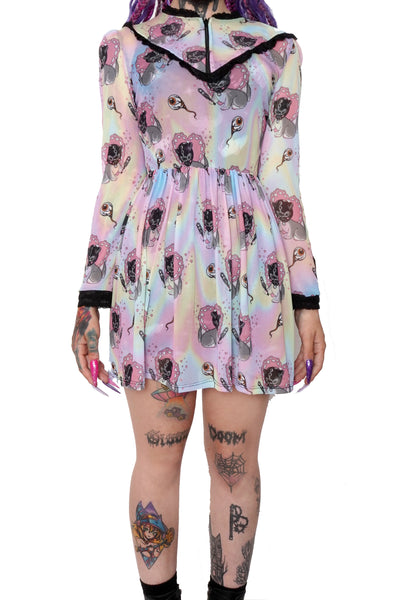 Pastel color Victorian style mesh dress with long sleeves, black lace trim neckline, black lace cuffs and black lace V shape detail from mid chest to shoulders. Zipper located from neckline to V shape trim on chest. Dress is cinched at waist. Print features images of gray cat wearing a black bondage gimp mask holding a paddle. Print also features eyeballs.