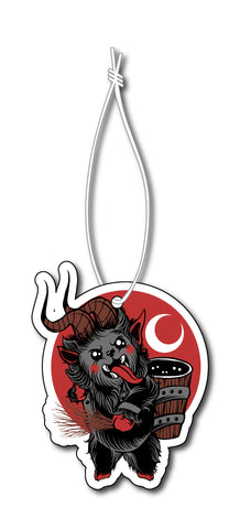 Air freshener with white elastic band. Features animated picture of Krampus sticking his tongue out with sticks in hand. Red background with white crescent moon.