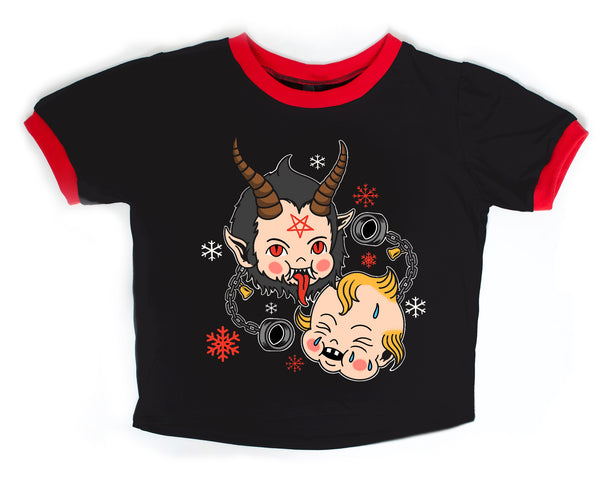 Black ringer tee with red trim. Features Krampus kewpie doll with red pentagram on forehead, sticking his tongue out. Another Kewpie crying and black chain handcuffs. Red and white snowflakes also on shirt.