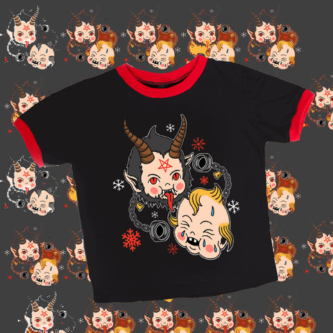 Black ringer tee with red trim. Features Krampus kewpie doll with red pentagram on forehead, sticking his tongue out. Another Kewpie crying and black chain handcuffs. Red and white snowflakes also on shirt.