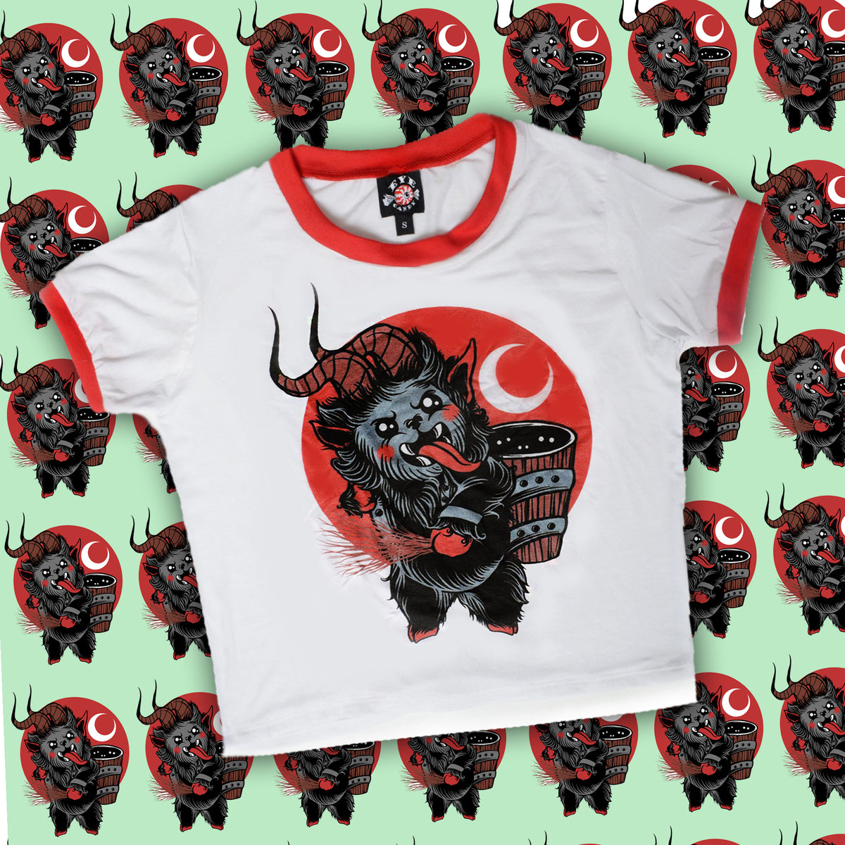 White ringer tee with red trim. Features animated Krampus sticking his tongue out while holding sticks in hand and wood pail on back. Red background with white crescent moon.