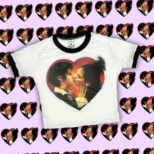 white ringer tee with black trim. Features Nancy from the movie "The Craft" and Lydia from "Beetlejuice" kissing inside a heart shape.