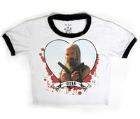 White ringer tee with black trim. Features picture of Otis from the movie "The Devil's Rejects" holding two guns across his chest inside a heart shape. Behind the heart there is red blood splatter and a banner on bottom of hearts that reads "OTIS" in black.