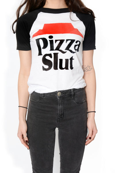 White baseball tee with black short sleeves and black trim neckline. Features image of red hat with black inscription "PIZZA SLUT".