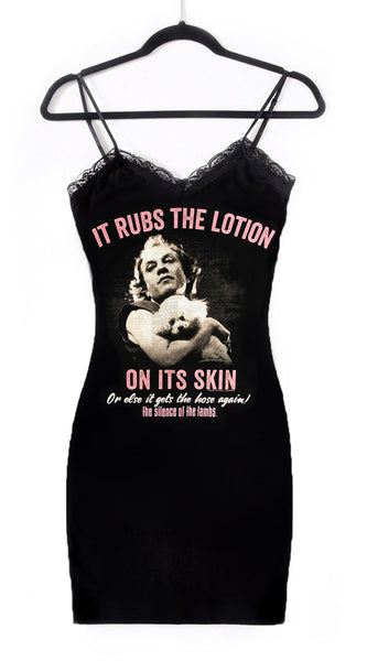 Black thin strap mini dress with black lace trim neckline. Features white print image of Ted Levine from the movie The Silence of The Lambs holding his white dog. Inscription reads "IT RUBS THE LOTION ON ITS SKIN OR ELSE IT GETS THE HOSE AGAIN!" in pink and white and "THE SILENCE OF THE LAMBS" in pink.