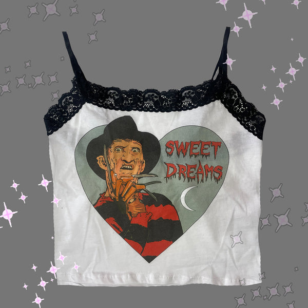 White tank top with thin black straps and black lace trim neckline. Features Freddy Krueger with one hand on face inside heart shape. Also features white crescent moon in heart shape. Inscription reads "SWEET DREAMS" in red. 