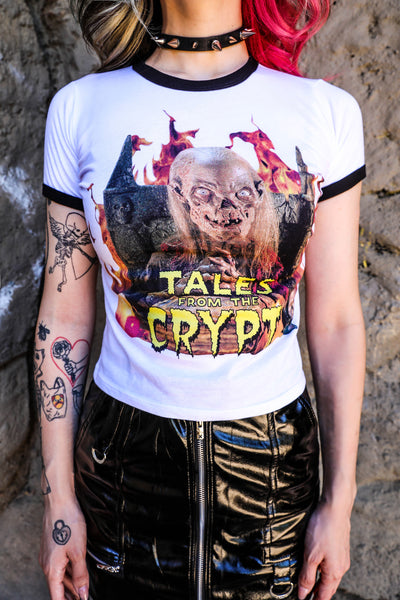White ringer tee with black trim. Features Skeleton sitting on thrown with hands clasped and flames in background. Inscription reads "TALES FROM THE CRYPT" in yellow.