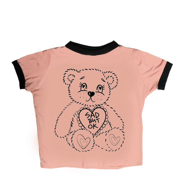 Baby pink ringer tee with black trim. Features a seated sad teddy bear with heart on chest. Inscription in heart reads "SAD BUT OK" in black.