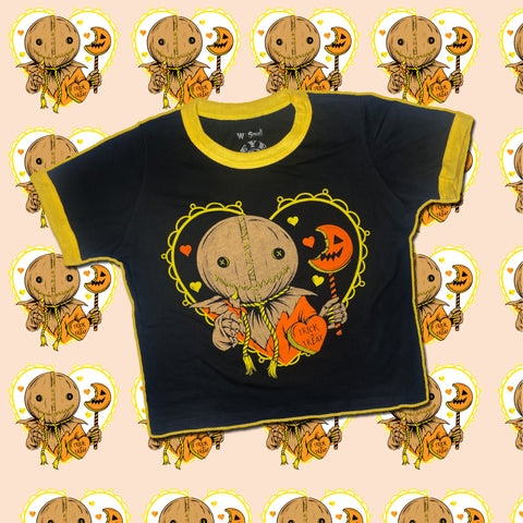 Black ringer tee with yellow trim. Features Sam from the movie Trick r Treat holding an orange jack o lantern lollipop that has been bitten with orange heart in front of him that reads "TRICK or TREAT" in black. Orange and yellow hearts in background. Image inside the outline of yellow heart.