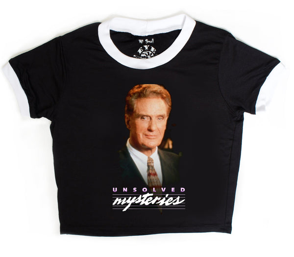 Black ringer tee with white trim. Features the host of Unsolved Mysteries, Robert Stack, smiling wearing a suit and tie. Inscription reads "Unsolved Mysteries" in purple and white.
