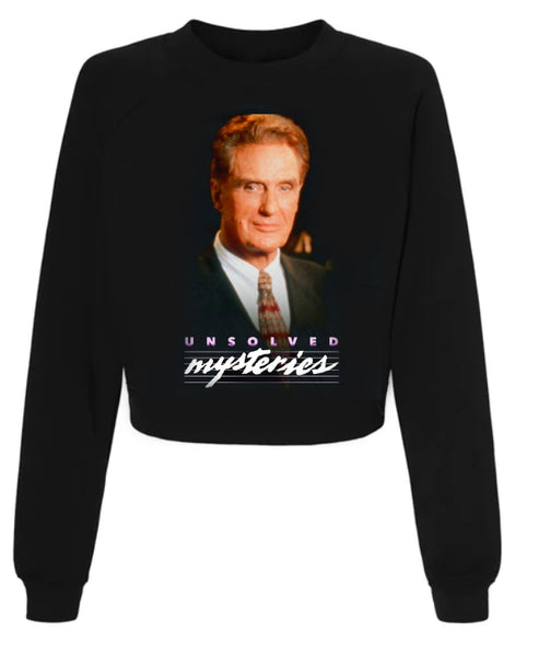 Black long sleeve pull over sweater. Features image of the host of Unsolved Mysteries, Robert Stack, smiling wearing a suit and tie. Inscription reads "Unsolved Mysteries" in purple and white.